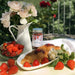 Frutteto Italia - Organic Strawberry Jam 6 x 250g on a table with fresh strawberries, a vase with flowers and a croissant topped with jam