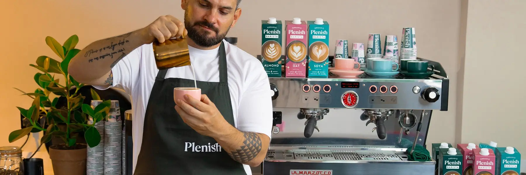 Plenish Barista making coffee in front of coffee machine and Plenish plant milks